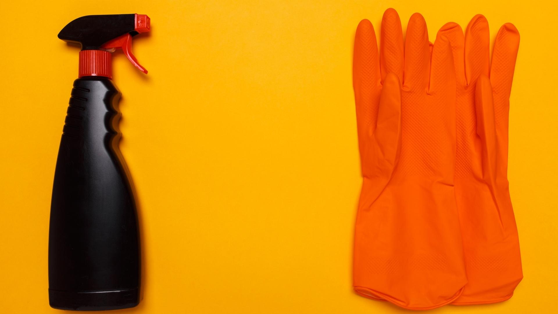 Orange nitrile gloves and ammonia based glass cleaner in a black spray bottle. Yellow background