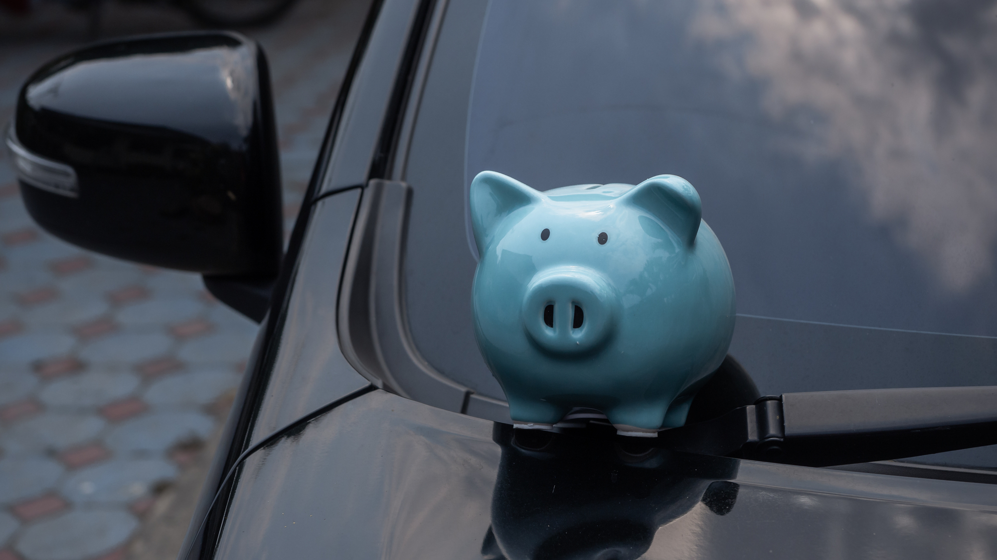 Piggybank on car's hood in a front of windshield