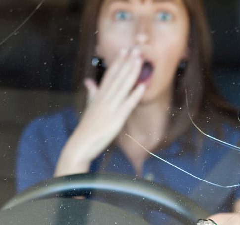Woman behind steering wheel is surprised by cracked windshield