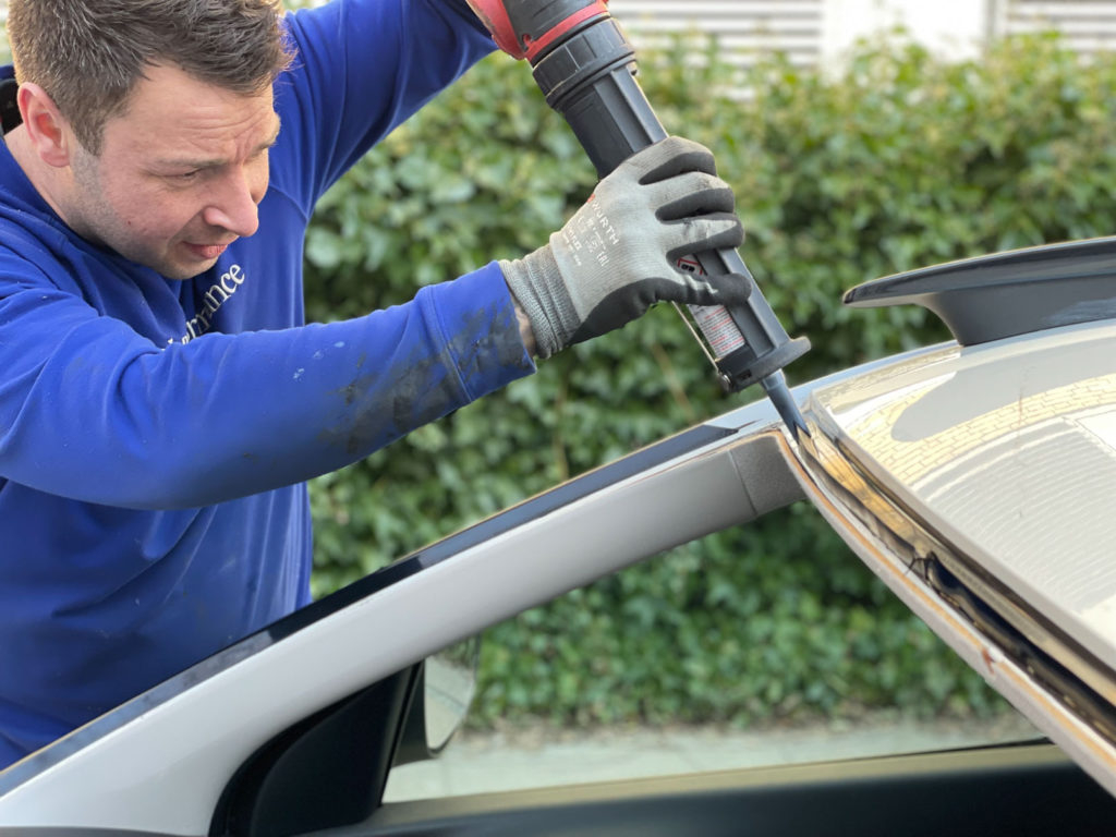 Professional auto glass technician applying urethane on car's pinch weld