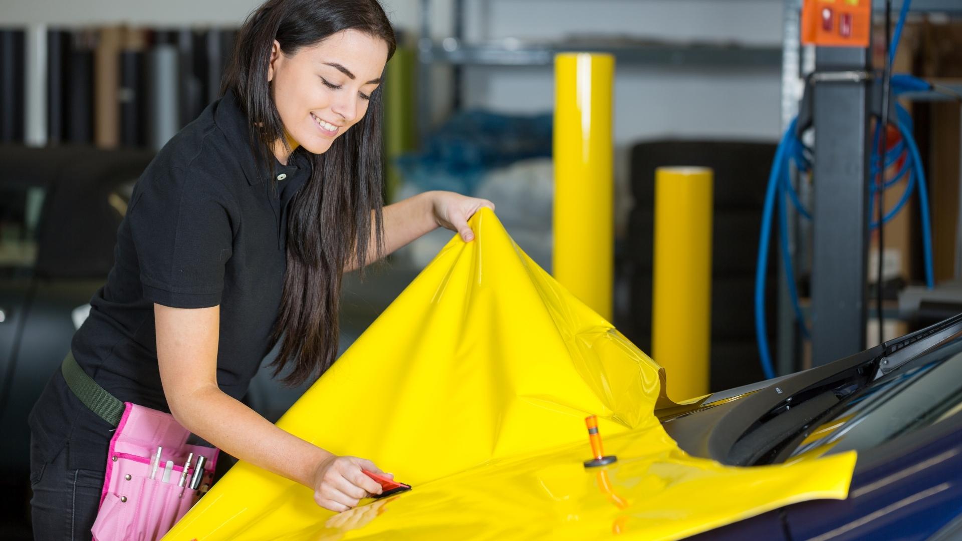 Woman is wrapping vehicle with bright yellow wrap, wrapping process