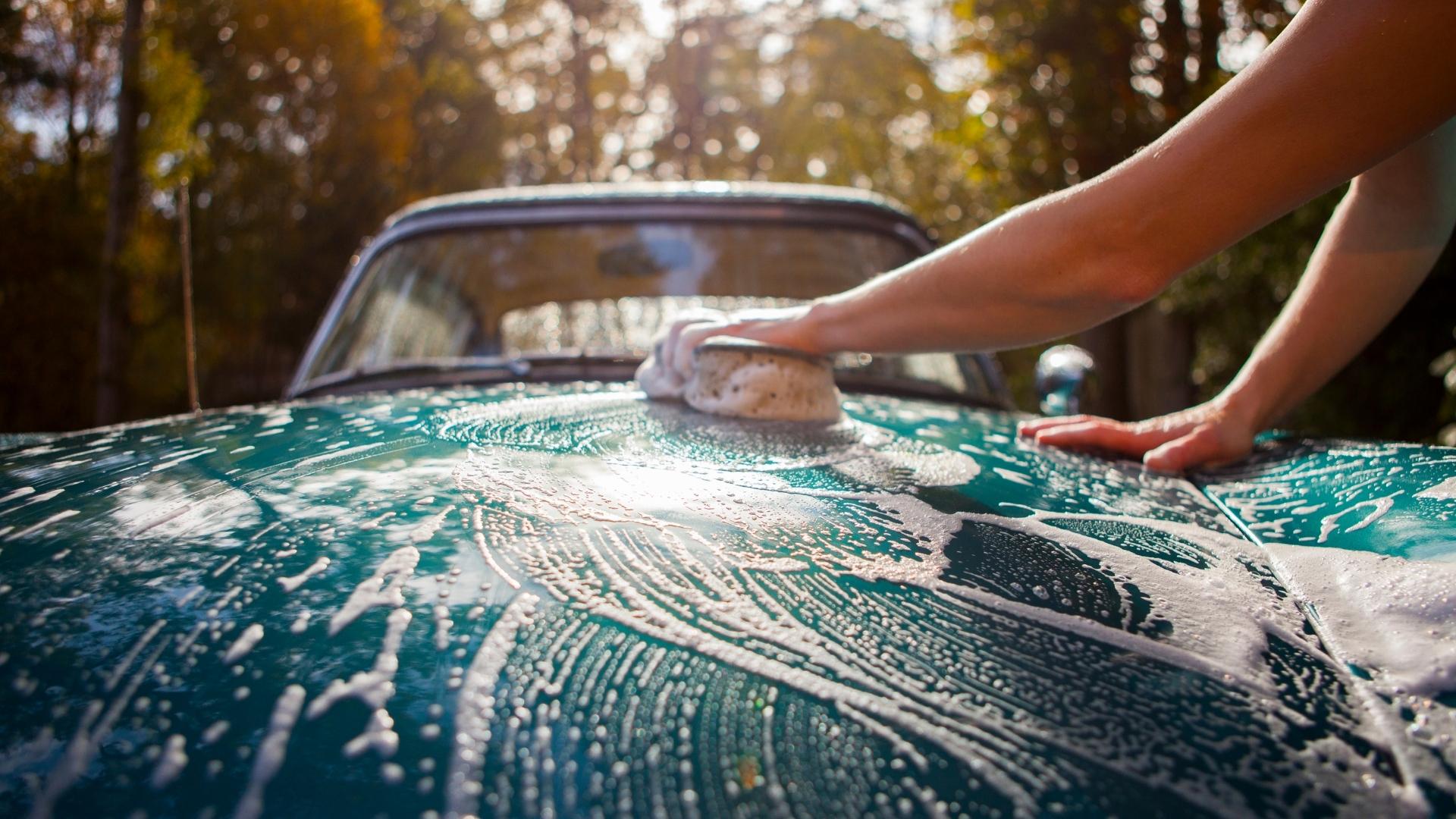 Person is washing classic green car with sponge and car shampoo